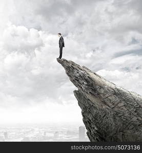 Risk in business. Young businessman standing on edge of rock mountain