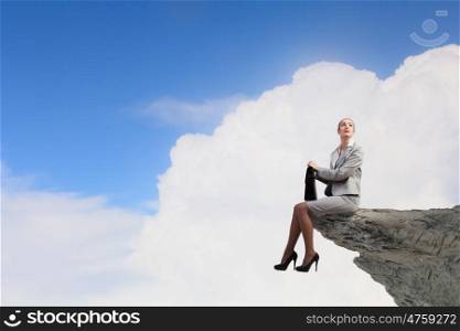 Risk in business. Young businesswoman with suitcase sitting on rock edge