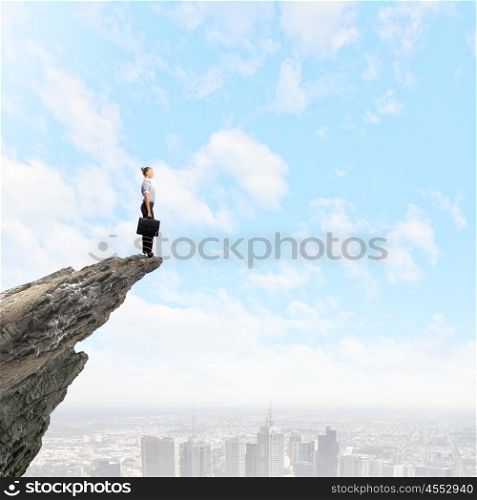 Risky business. Attractive businesswoman standing on edge of mountain