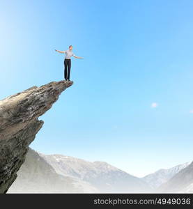 Risky business. Attractive businesswoman standing on edge of mountain