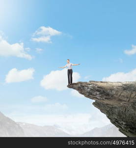 Risky business. Attractive businesswoman standing on edge of mountain