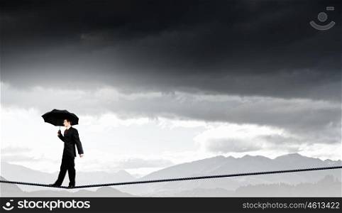 Risky business. Businessman with umbrella balancing on rope high on sky