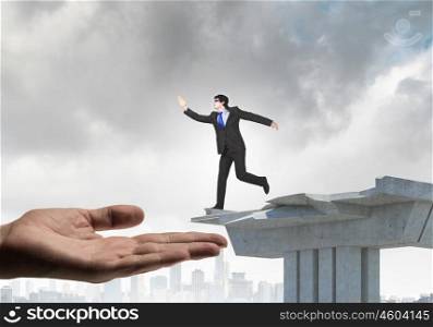 Risky business. Image of running businessman at the edge of bridge supported by human hand