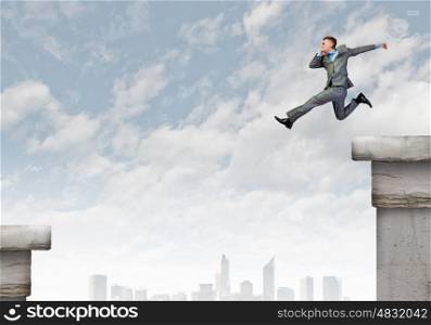Risky business. Young businessman jumping over gap. Risk concept