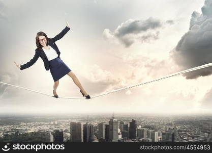 Risky business. Young businesswoman balancing on rope above city