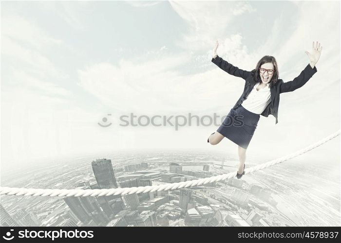 Risky business. Young businesswoman balancing on rope above city