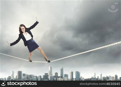 Risky business. Young businesswoman balancing on rope above city