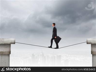 Risky businessman. Conceptual image of businessman walking on rope above gap