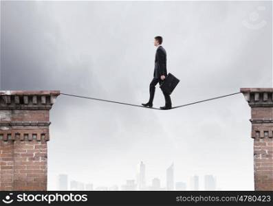 Risky businessman. Conceptual image of businessman walking on rope above gap