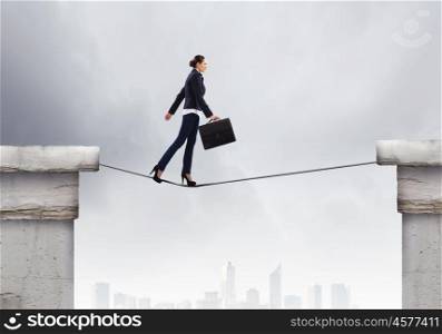 Risky businesswoman. Young confident businesswoman walking on rope above gap
