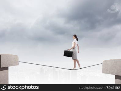 Risky businesswoman. Young confident businesswoman walking on rope above gap