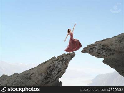 Risky step. Young woman in evening dress walking over mountain gap