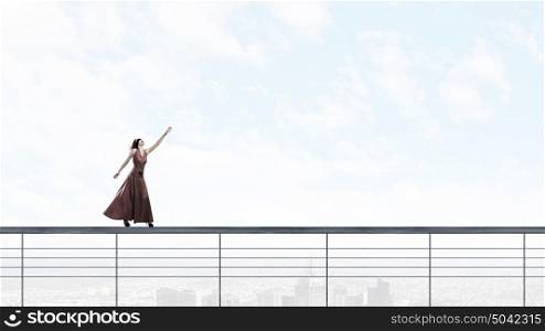 Risky woman. Woman in evening dress and blindfold walking on parapet