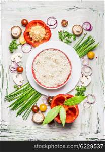 Risotto rice dish and various vegetables and seasoning ingredients for tasty vegetarian cooking on light rustic wooden background, top view composing. Healthy eating and diet food concept.