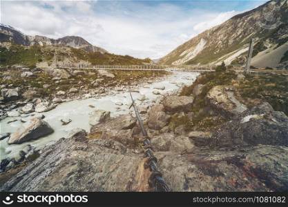 River and mountain landscape with bridge crossing the river. Beautiful nature scenery of rocky terrains. Shot in Mt Cook national park in New Zealand, South Island.
