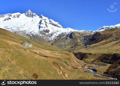 river crossing alpine valley with snowy peak mountain background under blue sky