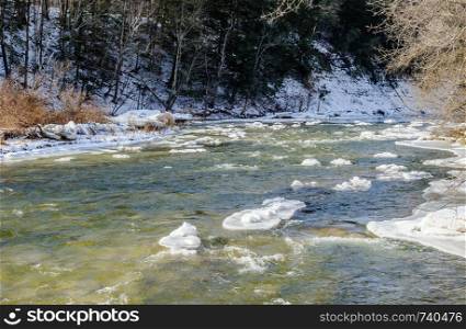 River flowing in winter with chunks of ice and snow.