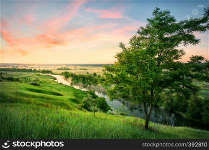 River in a valley with green grass under a dawn sky. Summer landscape. The concept of privacy travel and freedom. River in valley with green grass under dawn sky