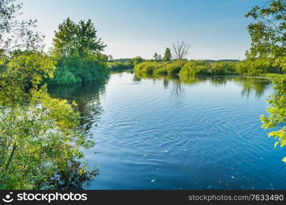 River landscape and green forest with trees blue water clouds on sky