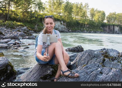 River selfie on mobile phone. Woman taking selfie on mobile phone with stick on mountain river background