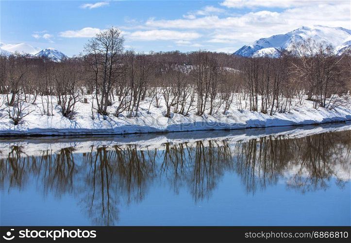 River, volcano, snow-covered forest and blue sky in early spring