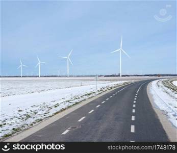 road and wind turbines near snow covered fields in dutch province of flevoland in the netherlands under blue sky