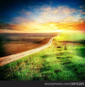 Road between the plowed and sown fields in the direction of setting sun. Road between the plowed and sown fields