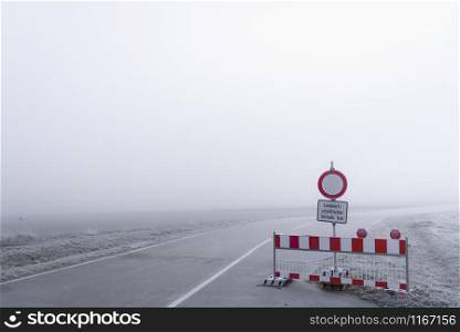 Road closed barrier on a cold foggy day in south Germany. Thick mist scenery. Road warning signs. German road safety