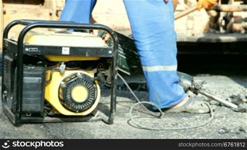 Road construction worker operates a phneumatic jack hammer to breakup asphalt on a road