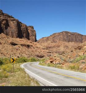 Road curving to right with red rock cliffs in Utah.