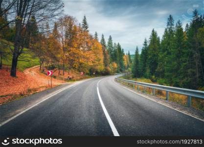 Road in autumn forest. Beautiful empty mountain roadway, trees with orange foliage and overcast sky. Landscape with asphalt road through the woods in fall. Travel in europe. Road trip. Transportation