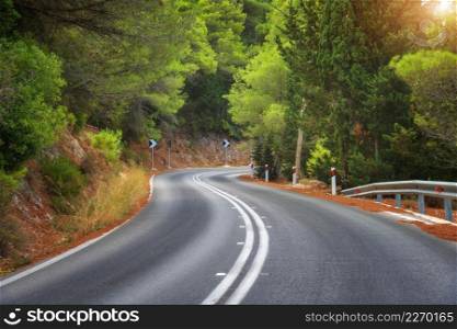 Road in green forest at sunset in summer. Beautiful empty mountain roadway, trees. Colorful landscape with road through the woods in spring. Travel in Greece. Road trip. Transportation. Highway