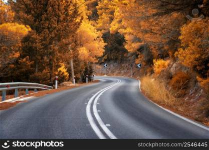 Road in orange forest at sunset in autumn. Beautiful empty mountain roadway and trees. Colorful landscape with road through the woods in fall. Travel in Greece. Road trip. Transportation. Highway