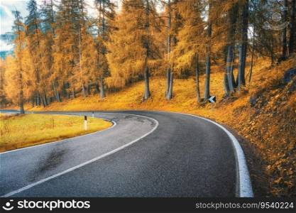 Road in orange forest at sunset in golden autumn. Dolomites, Italy. Beautiful mountain roadway, tress, grass, high rocks, blue sky with clouds. Landscape with empty highway through the woods in fall
