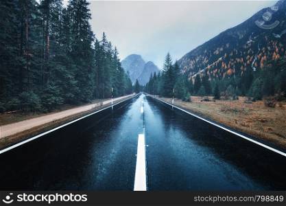 Road in the autumn forest in rain. Perfect asphalt mountain road in overcast rainy day. Roadway with reflection and trees in fog. Vintage style. Transportation. Empty highway in foggy woodland. Fall. Asphalt mountain road in foggy forest in overcast rainy day