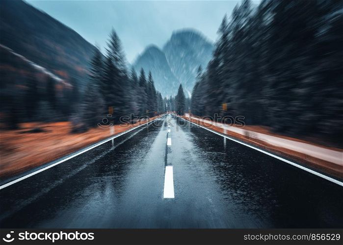 Road in the autumn forest in rain with motion blur effect. Perfect asphalt mountain road in overcast rainy day with blurred background. Roadway in motion. Transportation. Empty highway. Fast driving