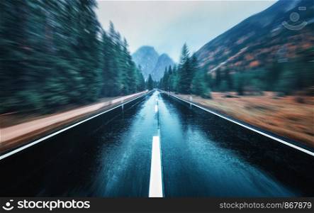 Road in the autumn forest in rain with motion blur effect. Perfect asphalt mountain road in overcast rainy day with blurred background. Roadway in motion. Transportation. Empty highway. Fast driving