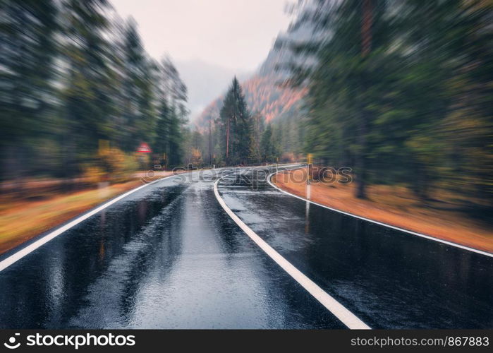 Road in the autumn forest in rain with motion blur effect. Perfect asphalt mountain road in overcast rainy day with blurred background. Roadway in motion. Transportation. Empty highway. Fast driving