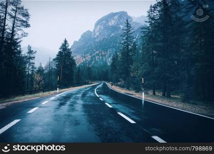 Road in the summer foggy forest in rain. Landscape with perfect asphalt mountain road in overcast rainy day. Roadway with reflection and green trees in fog. Vintage style. Empty highway. Travel. Road in the summer foggy forest in rain. Landscape