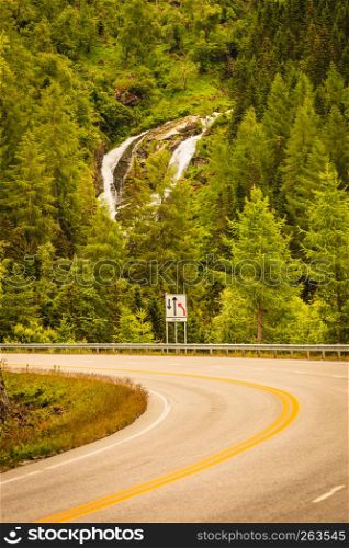 Road running through norwegian mountains. Beautiful landscape, green hiils with waterfall. Travel and tourism.. Road landscape in norwegian mountains