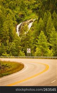Road running through norwegian mountains. Beautiful landscape, green hiils with waterfall. Travel and tourism.. Road landscape in norwegian mountains
