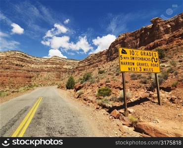 Road sign warning steep grade through rocky Utah landscape.