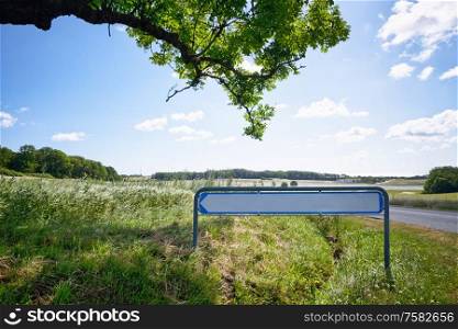 Road sign with an arrow in idyllic nature under a green tree in the summer