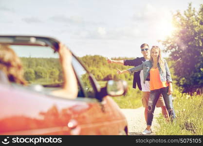 road trip, hitchhike, travel, gesture and people concept - happy couple hitchhiking and stopping car at countryside road. couple hitchhiking and stopping car on countryside