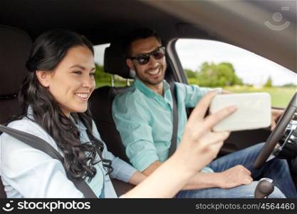 road trip, leisure, couple, technology and people concept - happy man and woman driving in car and taking selfie with smartphone