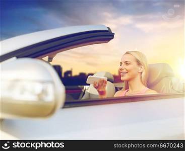 road trip, technology and communication concept - happy young woman calling on smartphone or using voice command recorder at convertible car over city sunset background. woman recording voice on smartphone at car. woman recording voice on smartphone at car