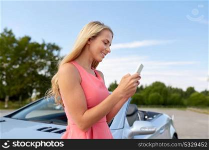 road trip, technology and communication concept - happy young woman with smartphone at convertible car. young woman with smartphone at convertible car