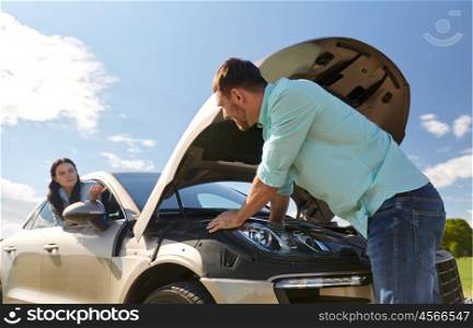 road trip, transport, travel and people concept - family couple with open hood of broken car at countryside