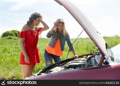 road trip, transport, travel and people concept - smiling young women with open hood of broken car at countryside