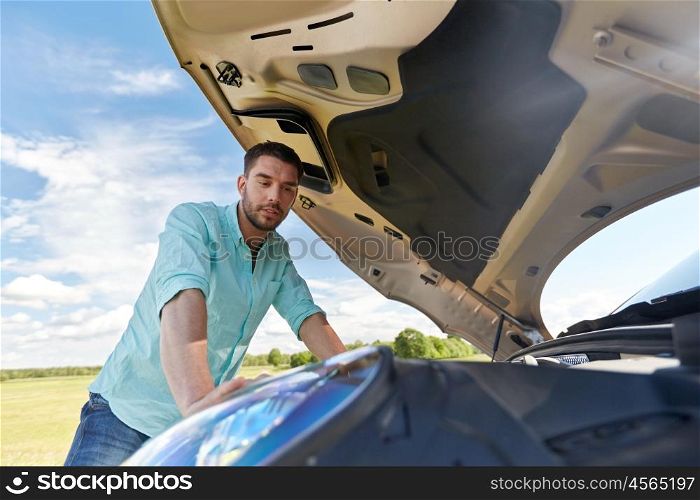 road trip, transport, travel and people concept - young man with open hood of broken car at countryside